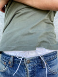 Close-up of white cotton boxer shorts with a board shorts-inspired elastic waistband and white drawstring, worn with a pair of blue jeans and khaki T-shirt.