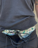 Close-up of Green and purple cotton boxer shorts with a board shorts-inspired elastic waistband and white drawstring, layered above back board shorts and black top