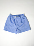 Light blue chambray boxer shorts with a board shorts-inspired design, featuring an elastic waistband, white drawstring, and relaxed fit.