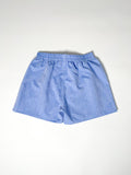 Light blue chambray boxer shorts with a board shorts-inspired design, featuring an elastic waistband, white drawstring, and relaxed fit.
